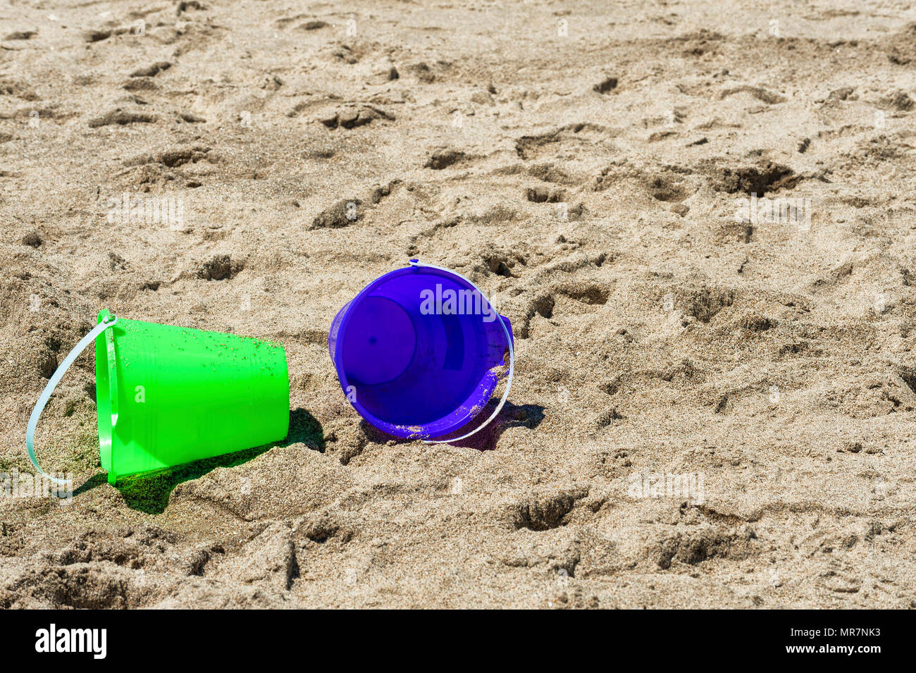 Closeup and copyspace of two play buckets one green the other purple left lying on sandy beach Stock Photo