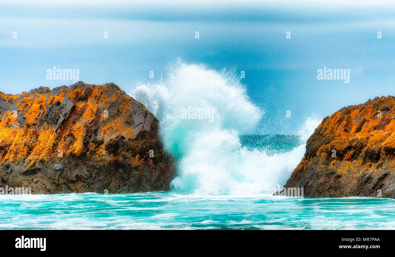 Two intertidal rocks frame a breaking wave along the shores of the ...
