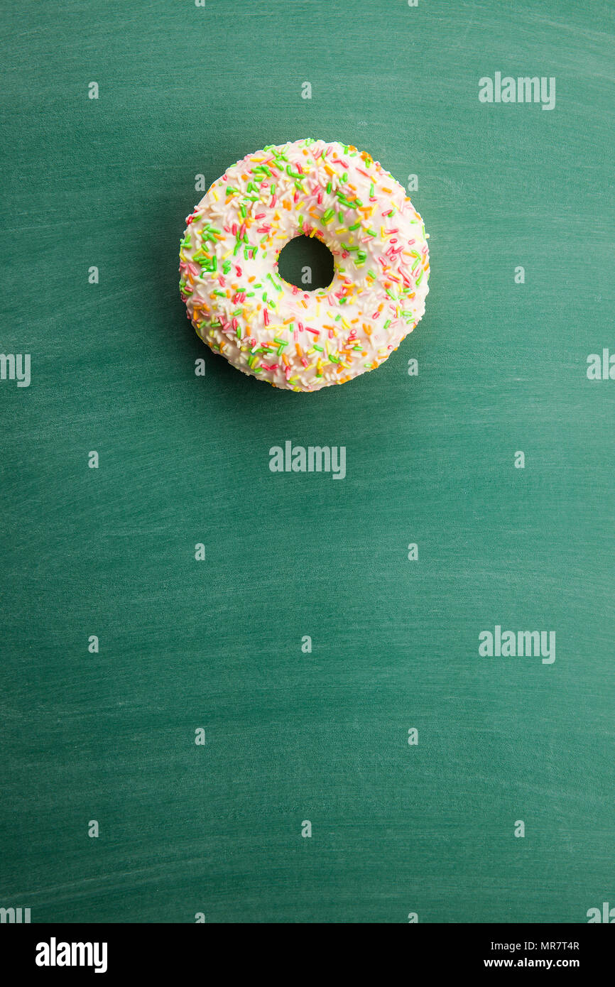 Sweet sprinkled donut on green chalkboard. Stock Photo