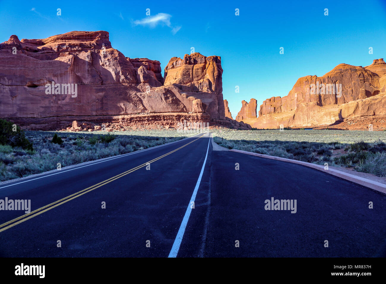 Road trip through the Arches National Park, Moab Utah. The black pavement of the road leads to the sandstone monuments and rock formations. Stock Photo