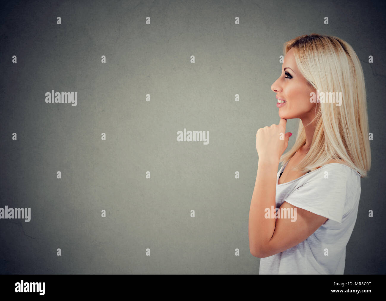 Side view of a pretty blonde woman in contemplation looking away thinking of idea on gray background. Stock Photo