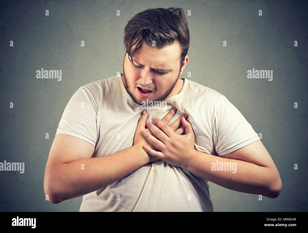 Young man with overweight holding hands on chest suffering with heart attack on gray backdrop. Stock Photo