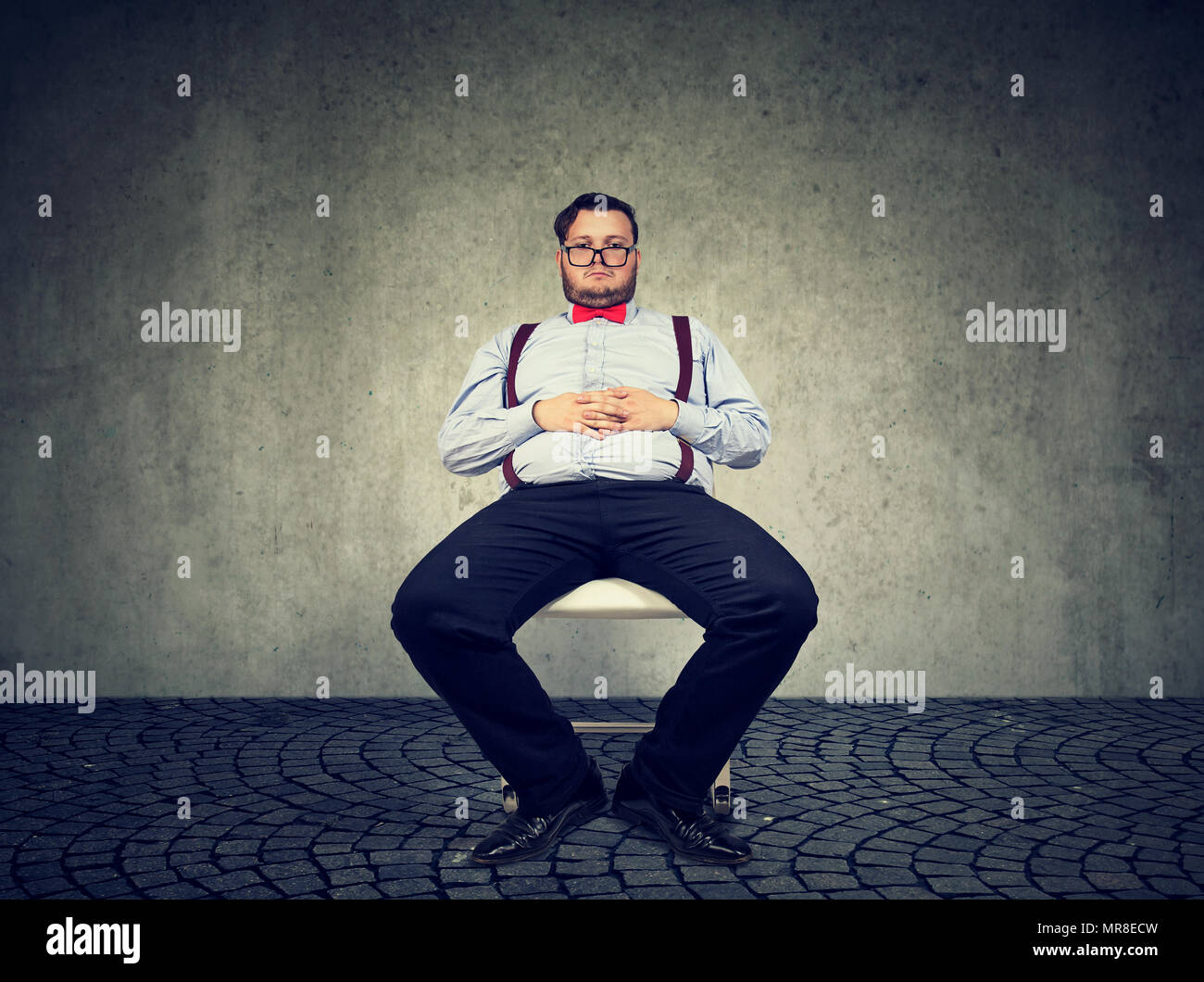 Obese man in formal outfit having sedentary way of living looking lazy on gray background. Stock Photo