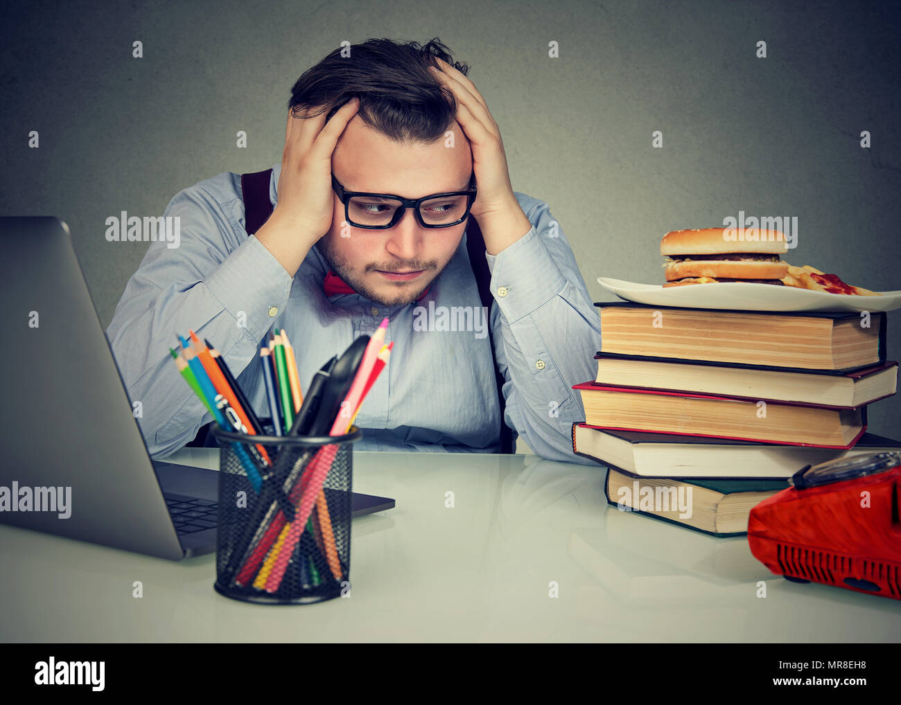 Overworked stressed chubby man sitting at desk and craving a burger Stock Photo