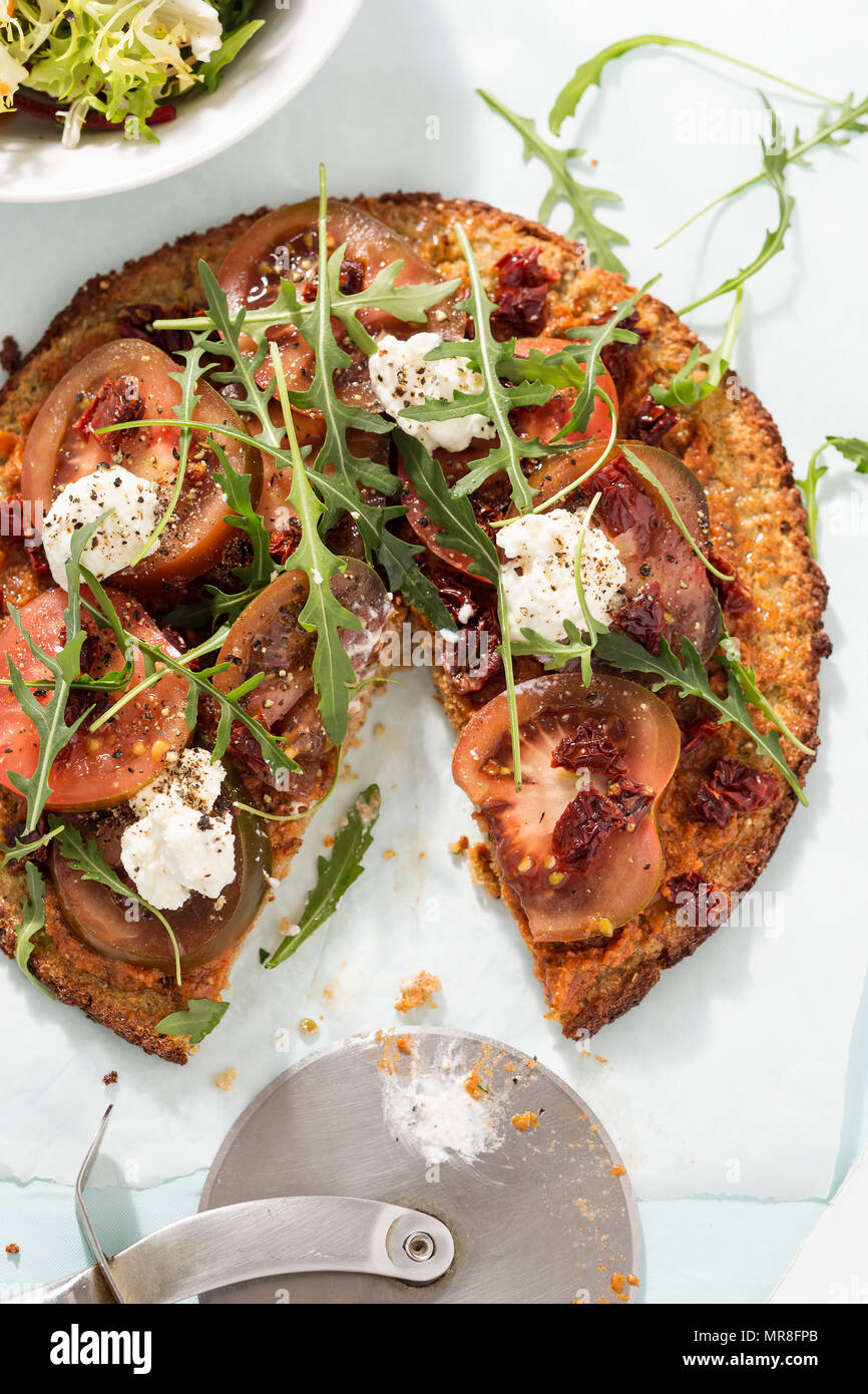 Healthy quinoa pizza with tomatoes, sun dried tomatoes, roquette leaves and goats cheese Stock Photo