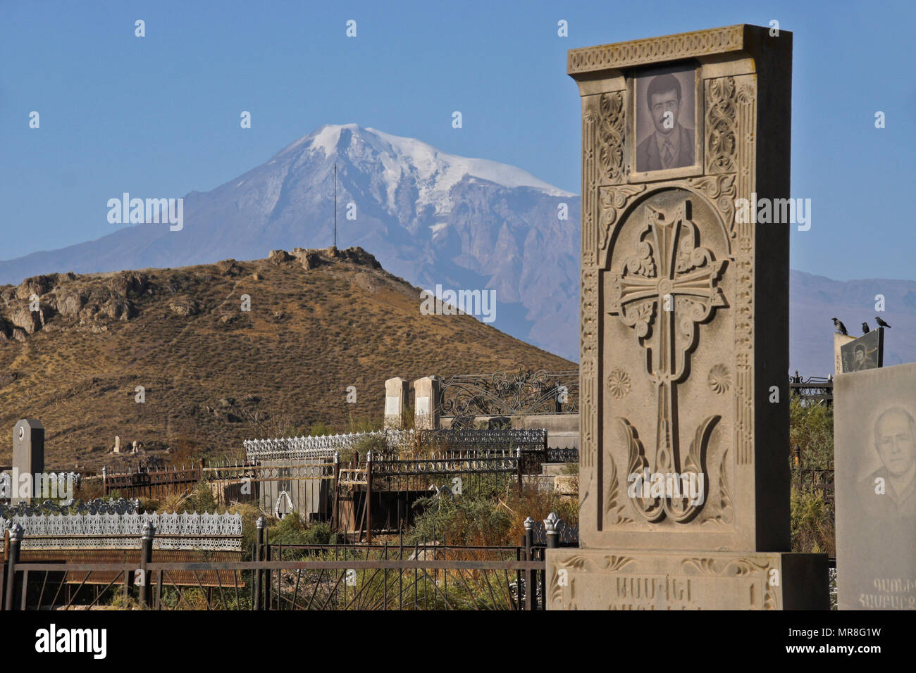 Mount Ararat looms behind a cemetery next to Khor Virap Monastery in Armenia. Many tombstones include photographs of the deceased. Stock Photo