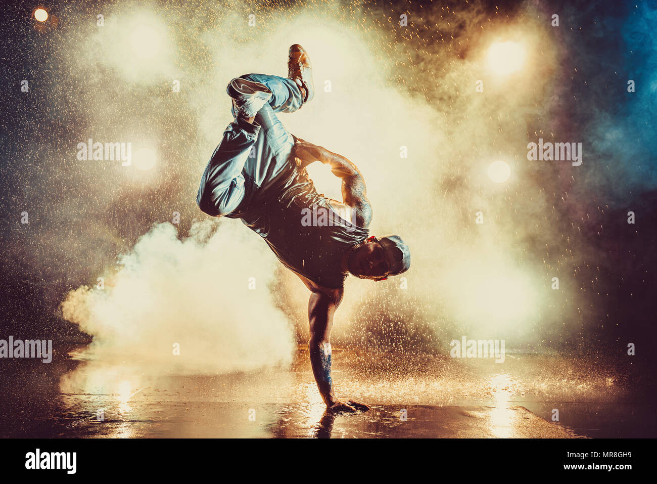 Young cool man break dancing in club with lights, smoke and water. Tattoo on body. Stock Photo