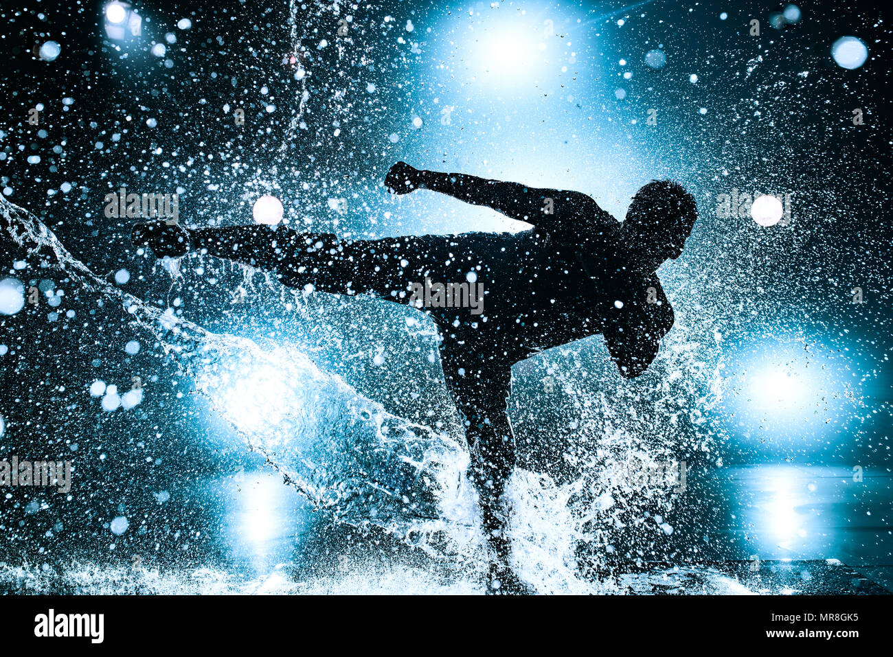 Young man break dancing in club with lights and water. Blue tint colors and dramatic silhouette. Stock Photo
