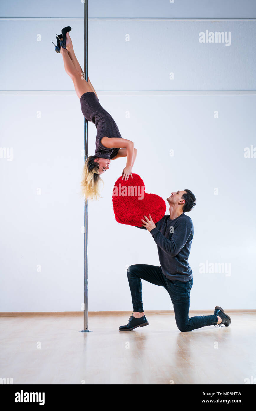 Young man and woman pole dancers. Man expressing feelings and giving big red heart. Love concept. Stock Photo