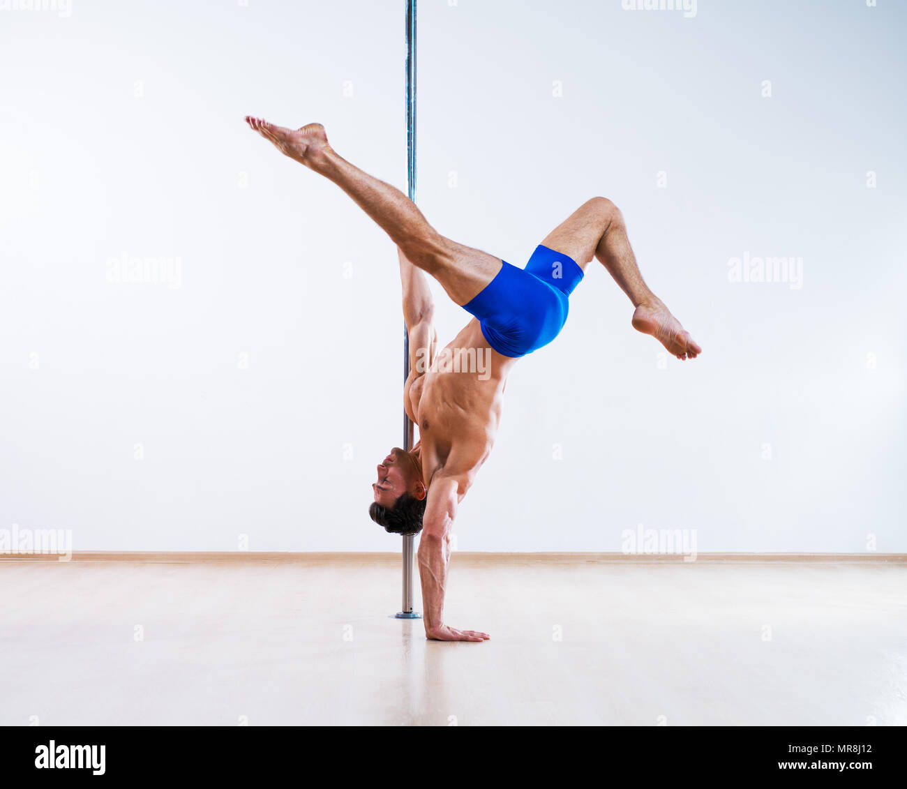 Young pole dancing man on white wall background Stock Photo