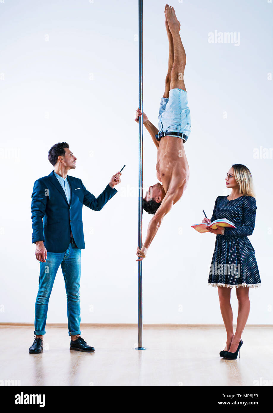 Young man teaching woman how to pole dance. One man is a teacher and a sportsman. Stock Photo