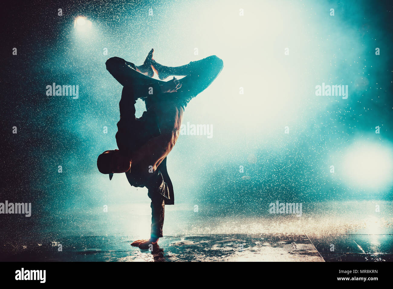 Young man break dancing in club with lights and water. Blue dramatic colors. Stock Photo