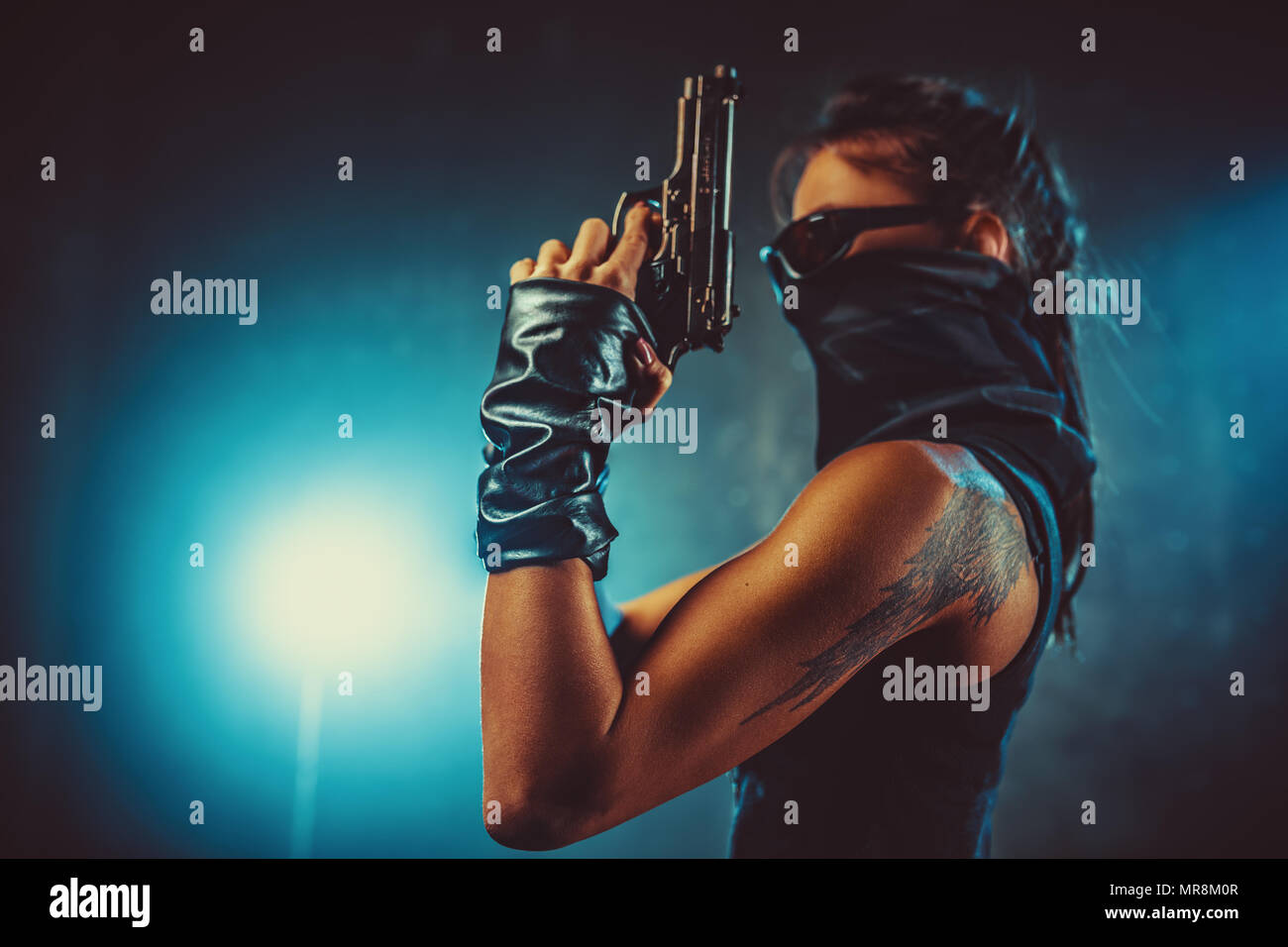 Dangerous woman fighter with gun and scarf in dark interior with smoke. Tattoo on body. Stock Photo