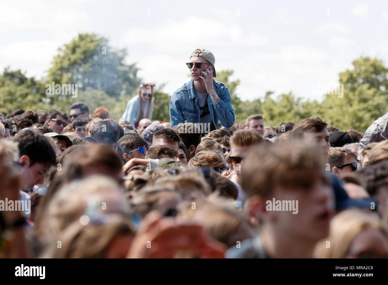 A young man on his phone while on a friend's shoulders at a music festival. Stock Photo