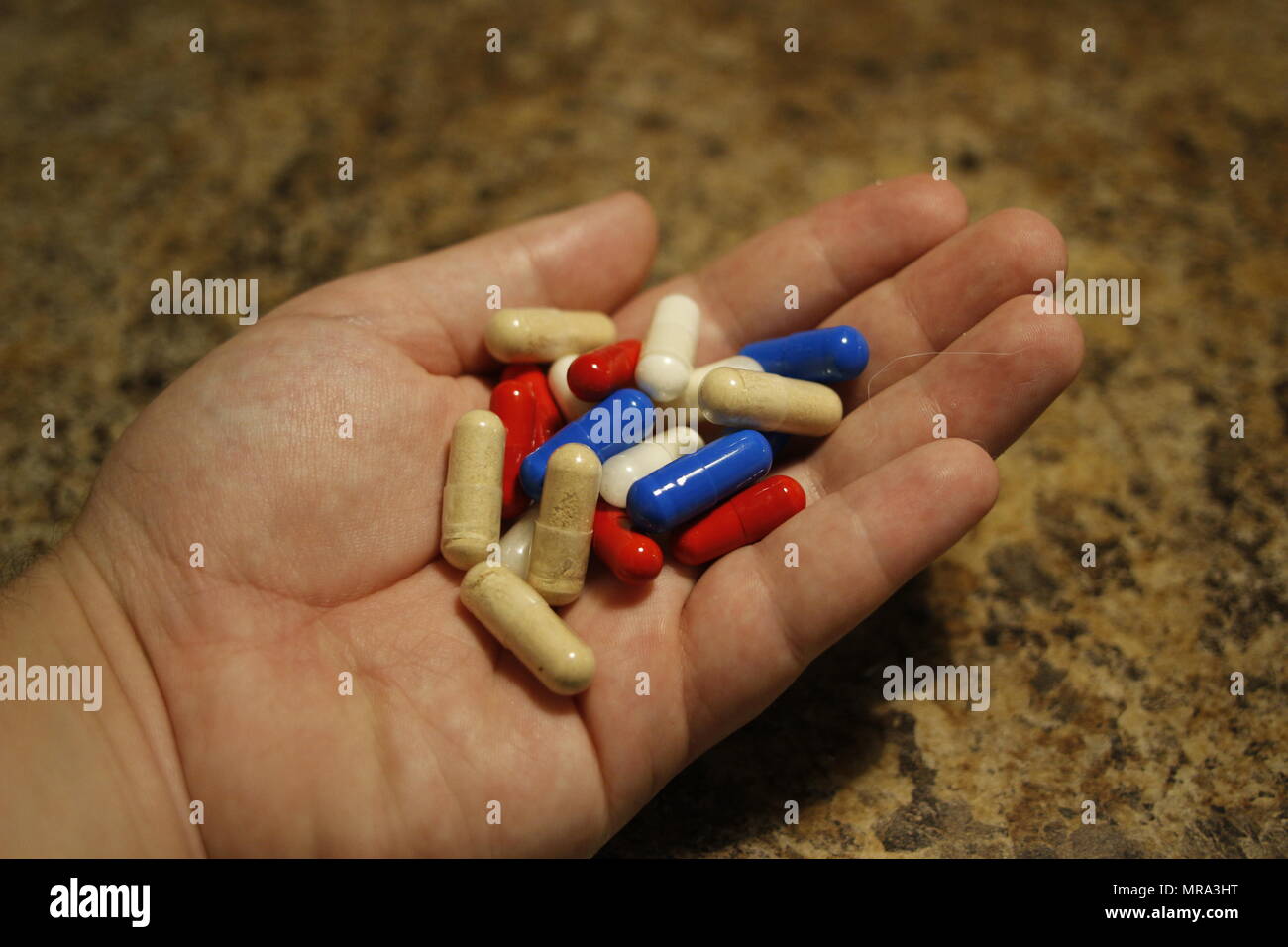 Various coloured pills in a hand isolated on marble backgroud. Stock Photo