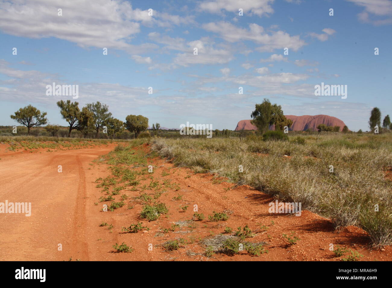 Dust trail through indigenous territory winds its way to Uluru in the distance. Stock Photo