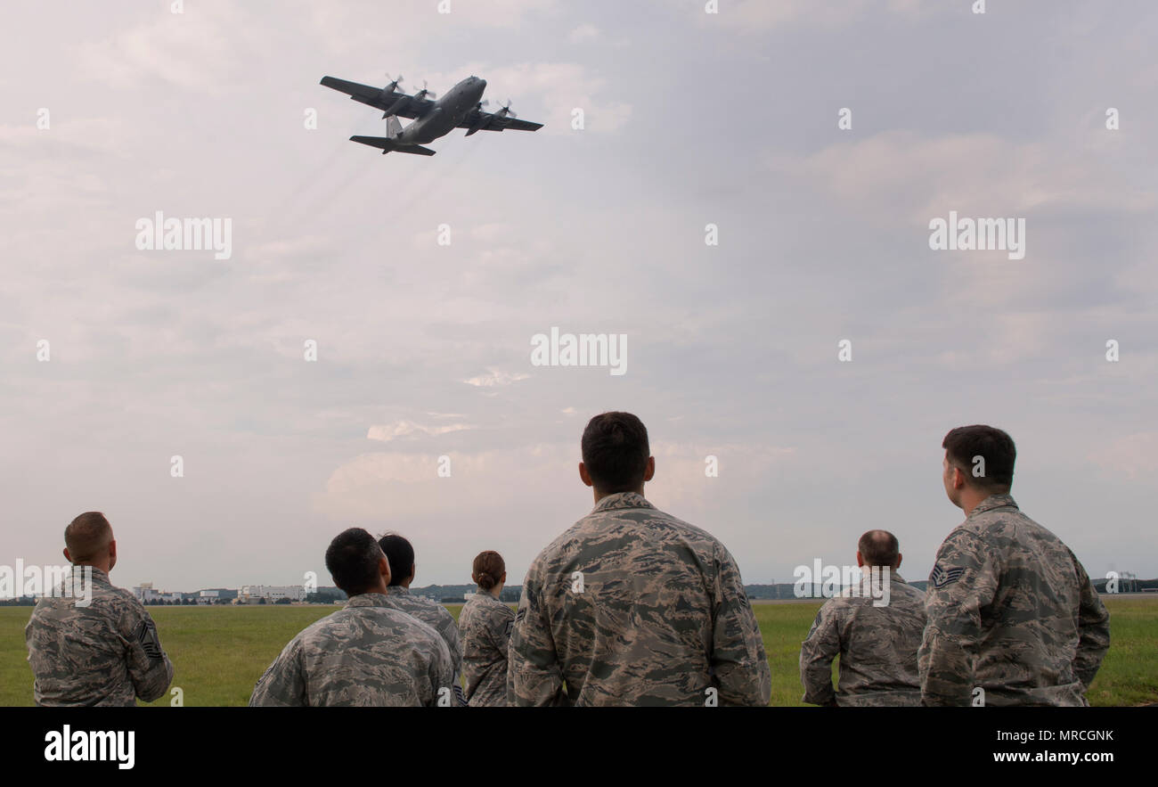 Members with the 374th Civil Engineer Squadron look up at a C-130 Hercules flying over the flightline during an annual certification test of the Aircraft Arresting System at Yokota Air Base, Japan, June 1, 2017. Airmen from the 374 CES and 374th Operations Support Squadron are responsible for setting up the system and logging any deficiencies during the test. (U.S. Air Force photo by Yasuo Osakabe) Stock Photo