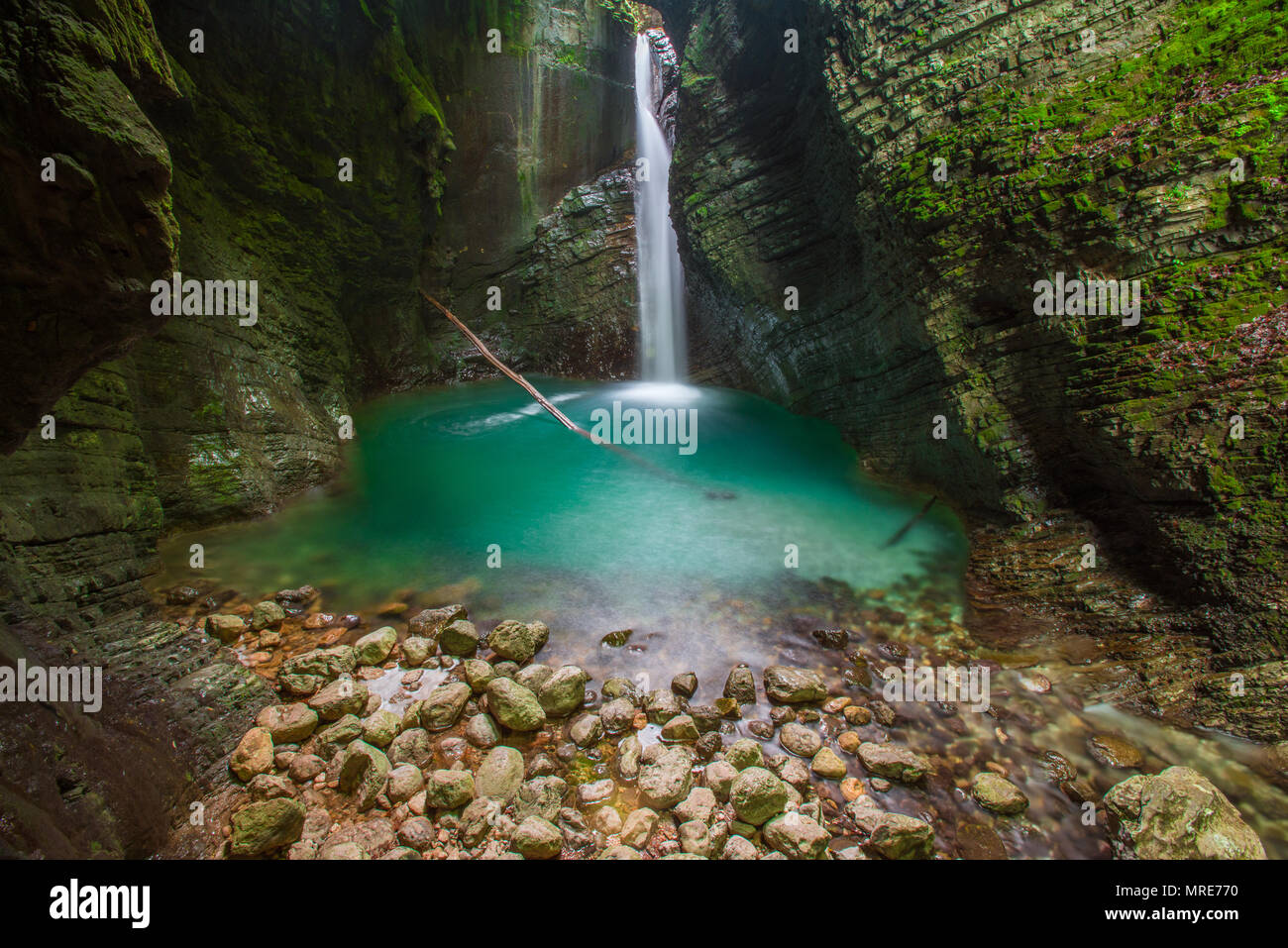 Hidden Kozjak waterfall streams out of layered, mossy rocks in a deep gorge.Blue water, insane crystal clear pool, rocks and dead tree. Long exposure. Stock Photo