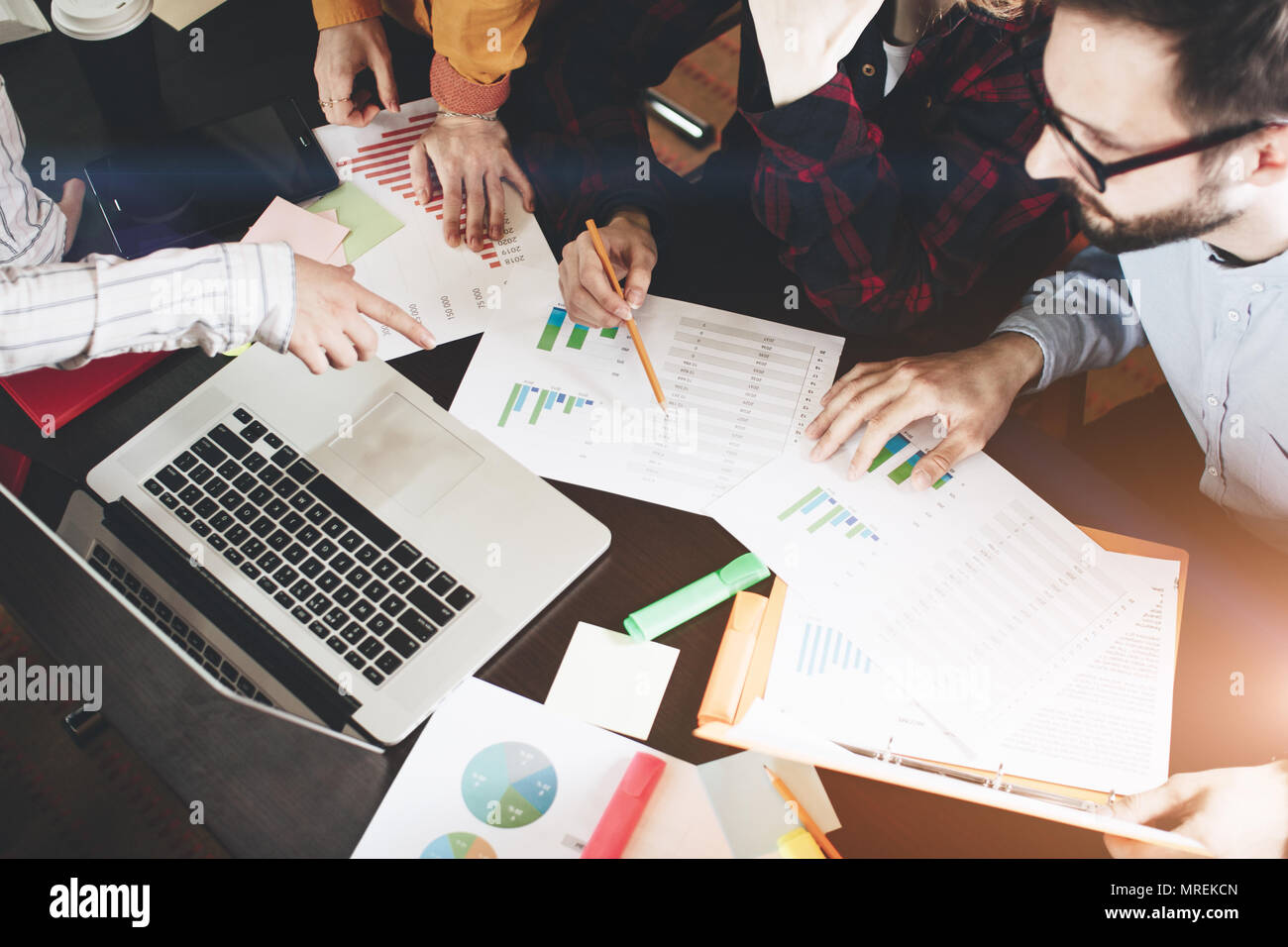 Young coworkers discussing  charts and graphs showing the results of their successful teamwork.  Laptop and paperwork on the table Stock Photo