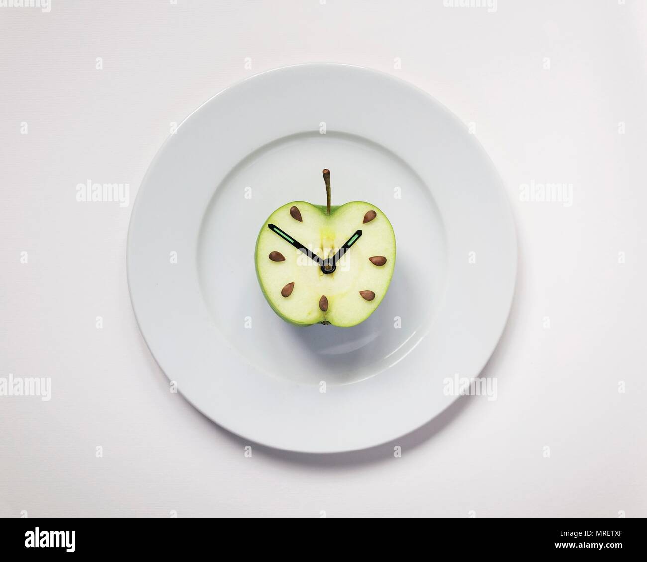 Half an apple on plate with clock hands, studio shot. Stock Photo