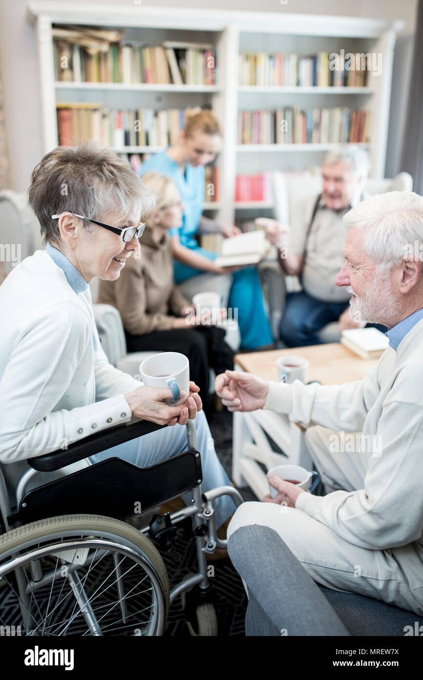 Senior woman in wheelchair talking to male fiend in care home. Stock Photo