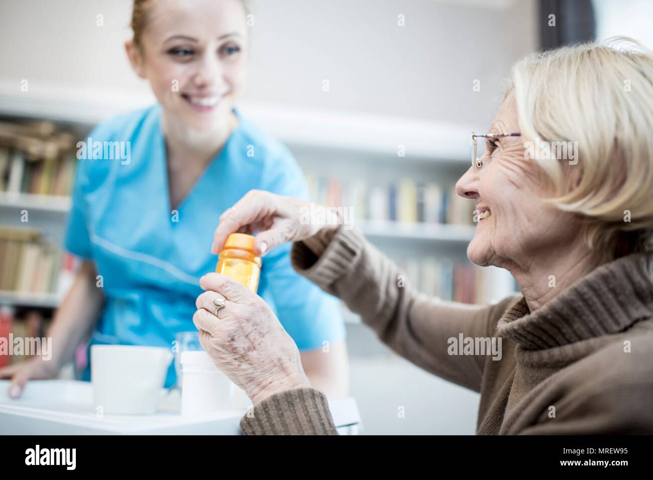 Care worker and senior woman opening medicine bottle. Stock Photo