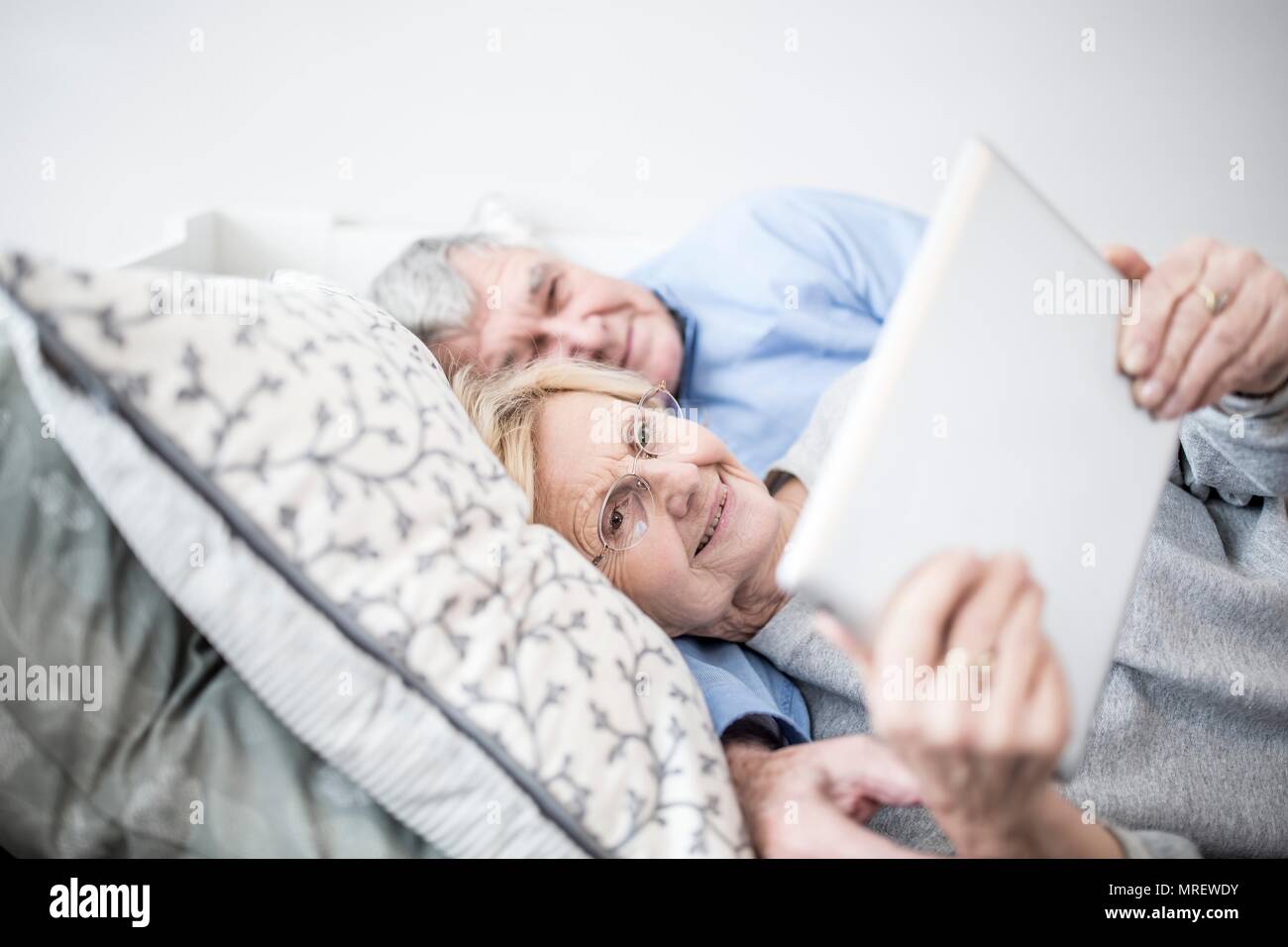 Senior couple lying down watching digital tablet. Stock Photo