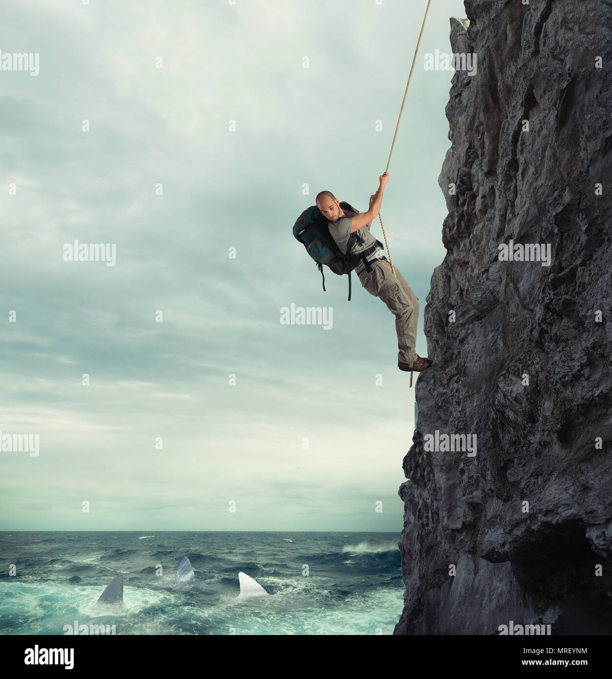 Explorer climbs a mountain with the risk to fall on the sea with sharks Stock Photo