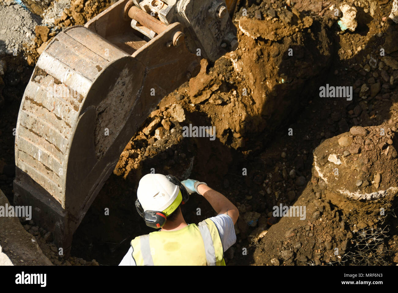 A construction worker directing the driver of an excavator digging the foundations for a new office development in Pontypridd town centre Stock Photo