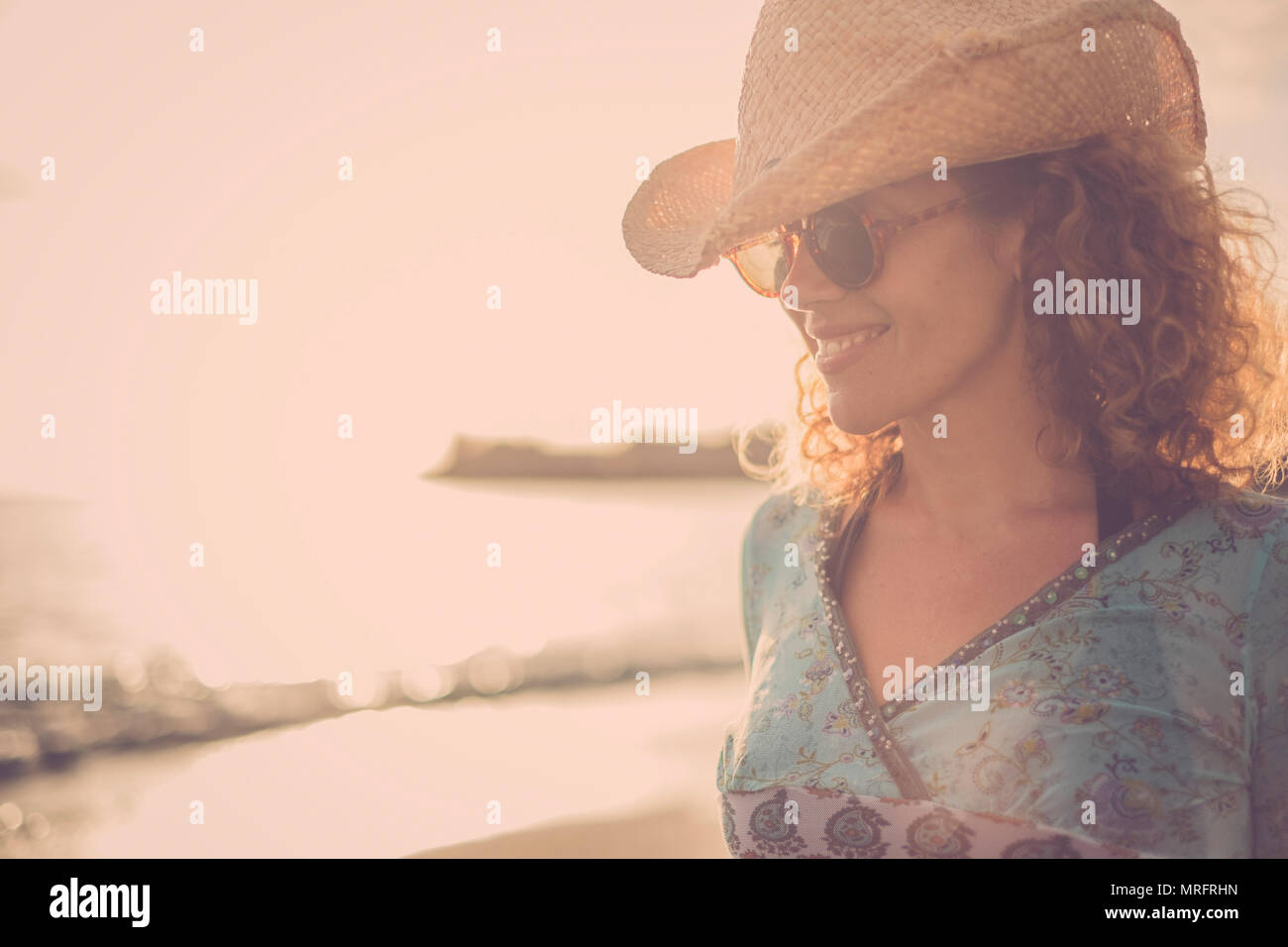 beautiful and wonderful blonde curly hair model middle age with cowboy hat smile and pose at the beach with golden sunset in the background. colored a Stock Photo