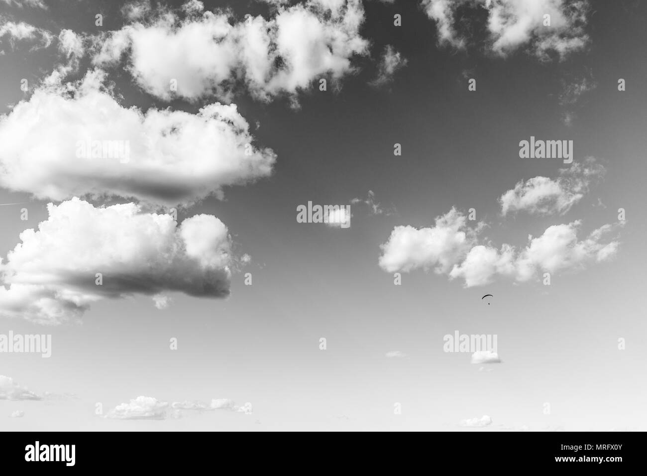 A paraglider flying against a beautiful. deep sky, with big white clouds Stock Photo