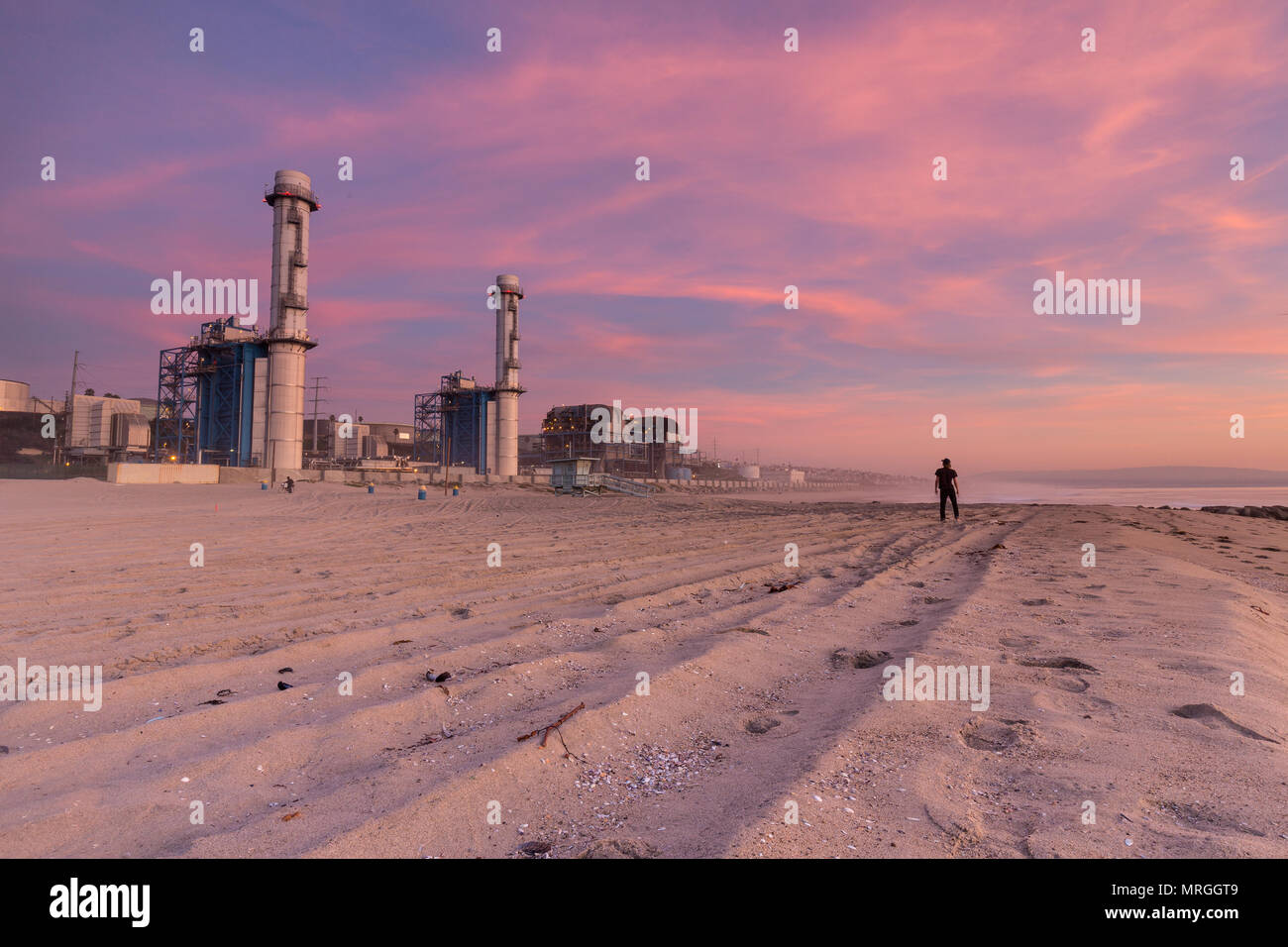 A stands on the sand dwarfed by the NRG Energy plant at El Porto Beach in Los Angeles. Stock Photo
