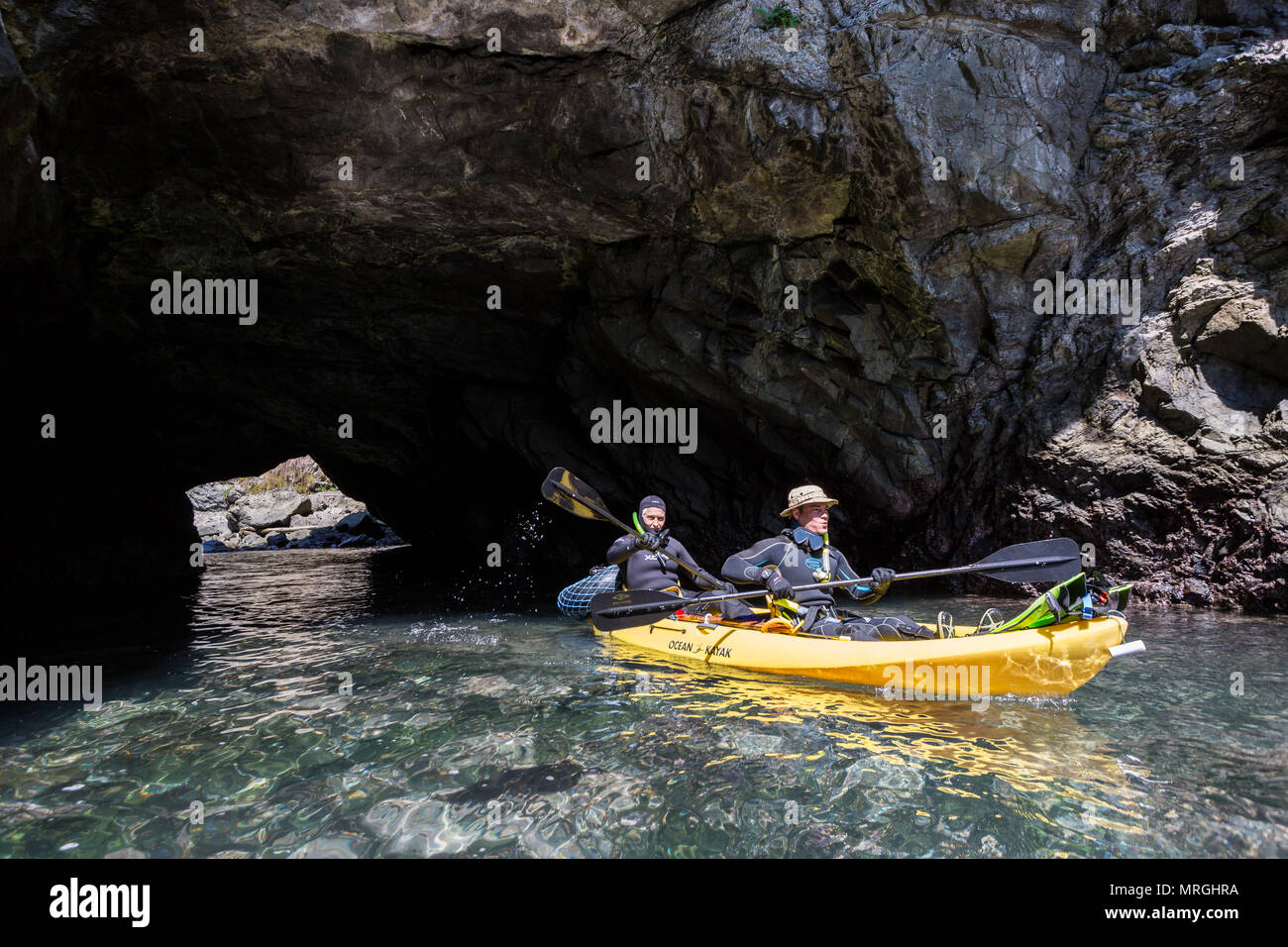 Two kayakers paddle through a sea arch near Russian Gulch State Park, clad in wetsuits for freediving. Stock Photo