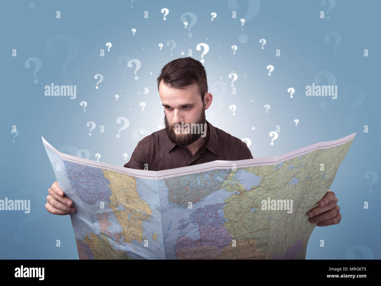 Handsome young man holding a map with white question marks above his ...