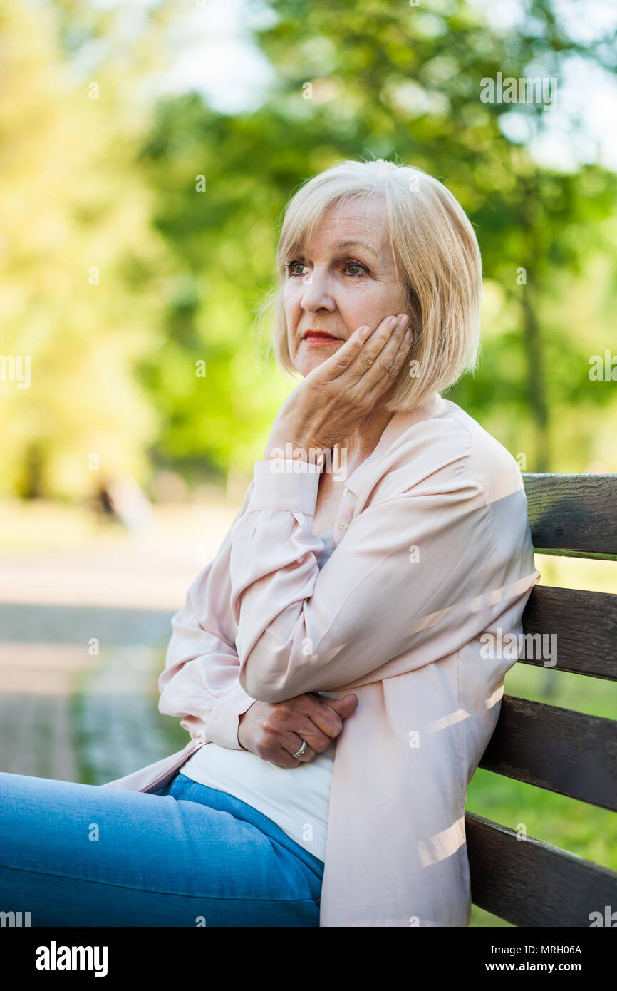 Lonely adult woman sitting in park in despair. Stock Photo