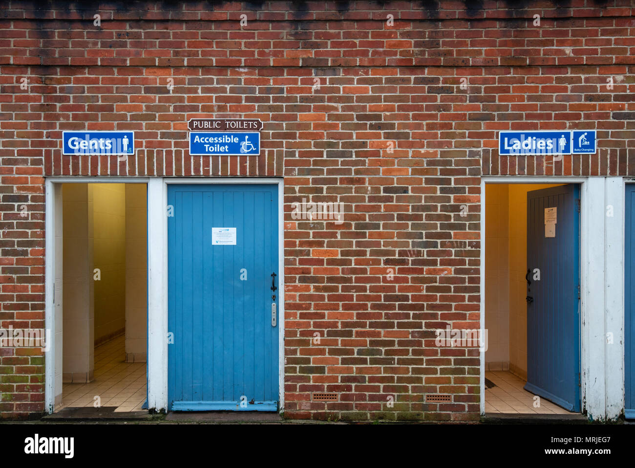 Public Toilets, Ladies, Gents and Accessible toilets with blue wooden doors in an old red brick building. Stock Photo