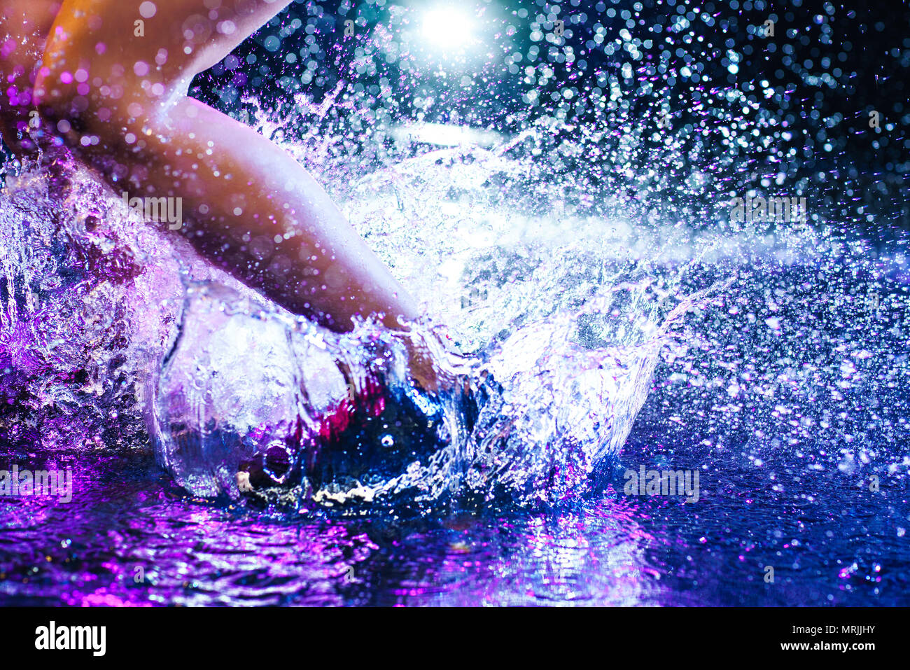Woman jumping on water with big splashes. Legs and shoes close-up. Studio with rain and drops interior. Stock Photo