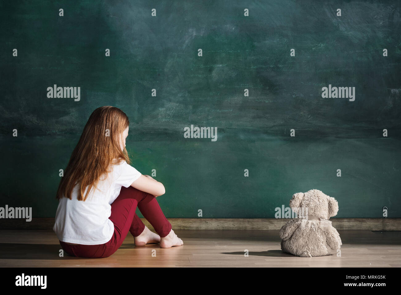 Little girl with teddy bear sitting on floor in empty room. Autism ...