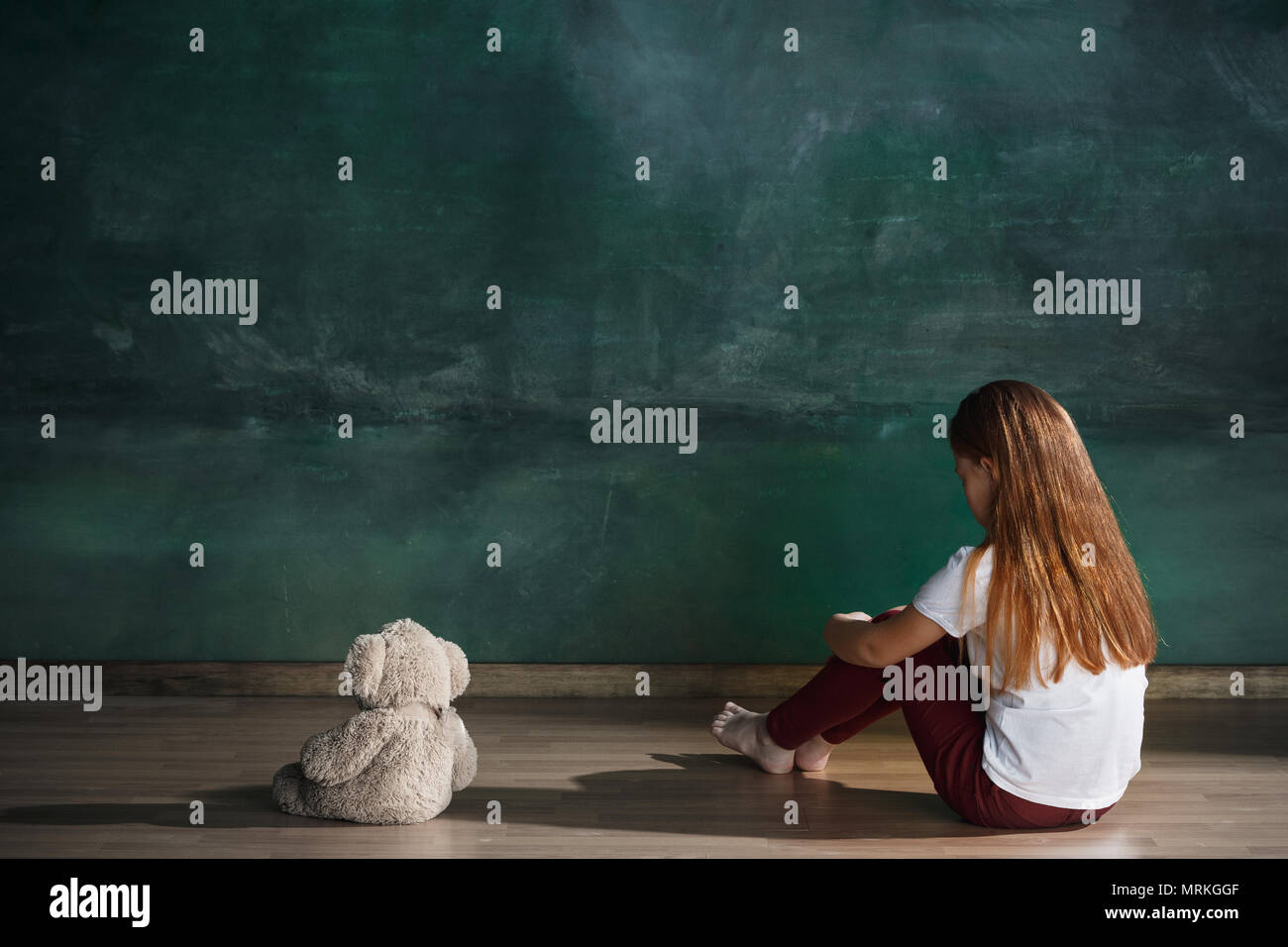 Little girl with teddy bear sitting on floor in empty room. Autism ...