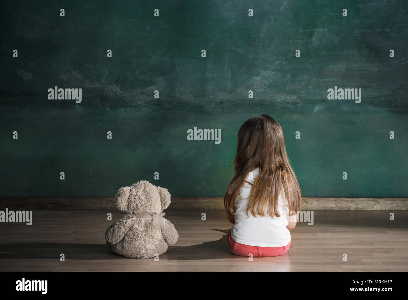 Little girl with teddy bear sitting on floor in empty room. Autism ...