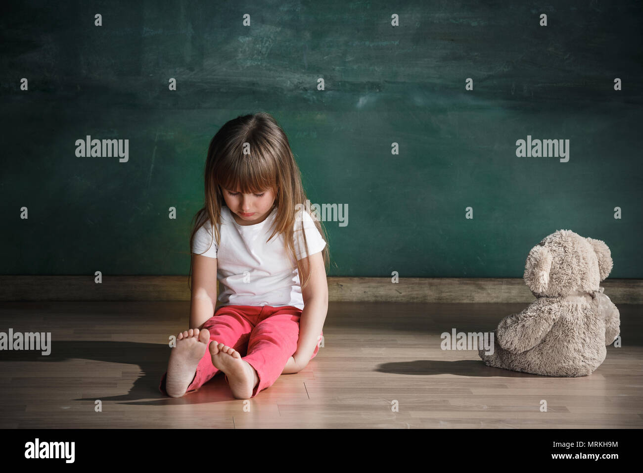 Little girl with teddy bear sitting on floor in empty room. Autism ...