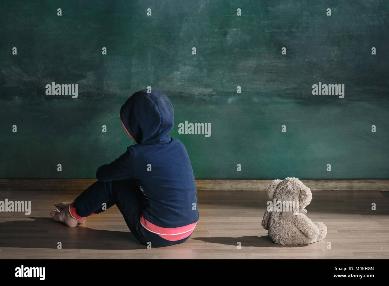 Little girl with teddy bear sitting on floor in empty room. Autism ...