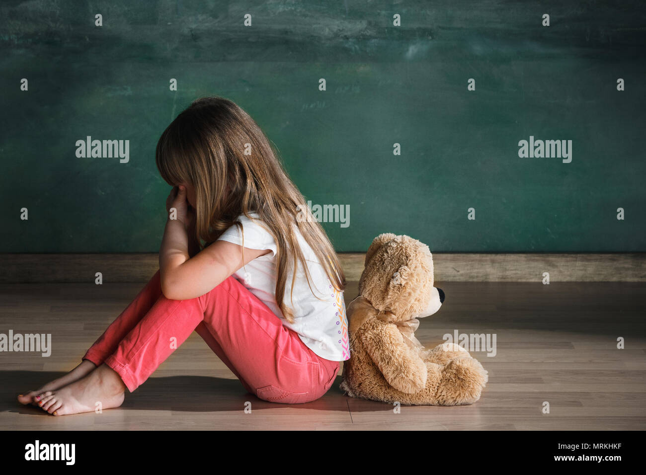Little girl with teddy bear sitting on floor in empty room. Autism ...