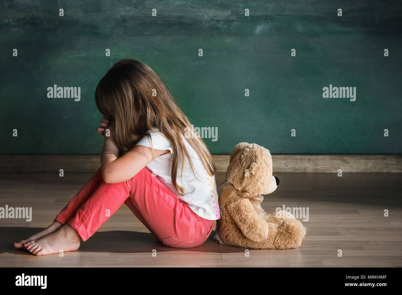 Little girl with teddy bear sitting on floor in empty room. Autism ...