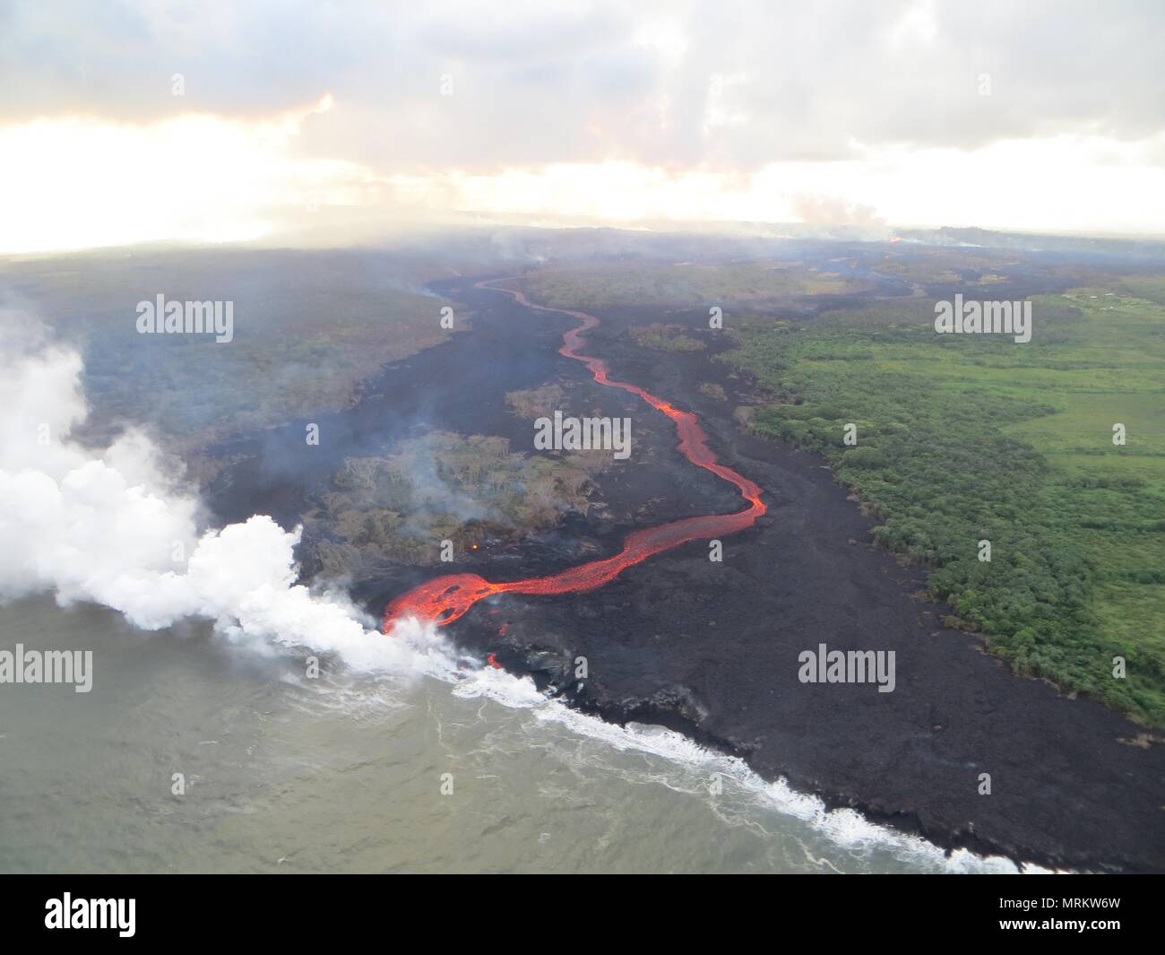Lava and poisonous sulfur dioxide plumes rise as molten magma reaches the ocean from the eruption of the Kilauea volcano May 23, 2018 in Pahoa, Hawaii. Hot lava entering the ocean creates a dense white plume called 'laze' (short for 'lava haze'). Laze is formed as hot lava boils seawater to dryness. The process leads to a series of chemical reactions that create a billowing white cloud composed of a condensed seawater steam, hydrochloric acid gas, and tiny shards of volcanic glass. The cloud is as corrosive as dilute battery acid, and should be avoided. Stock Photo