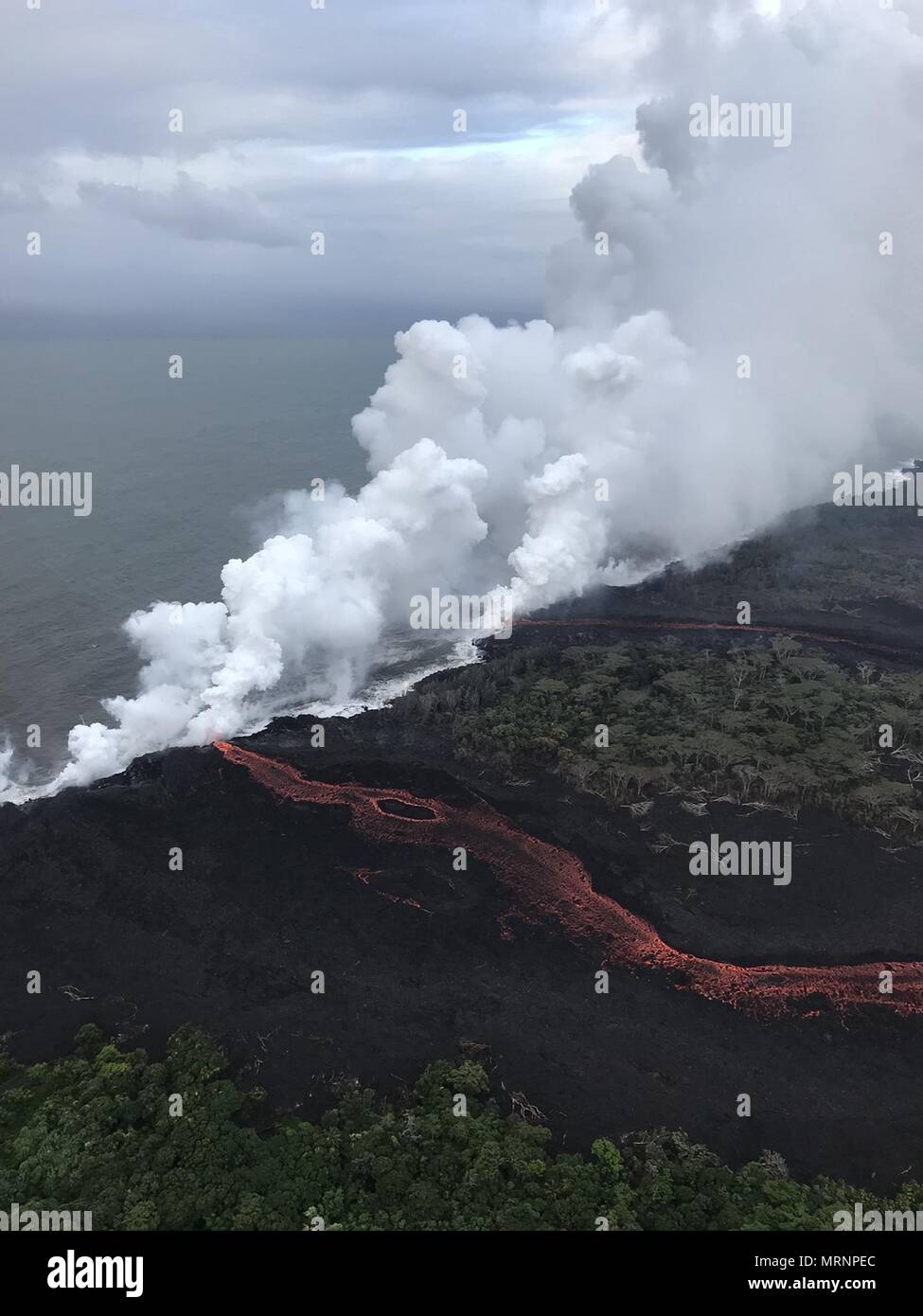 Lava and poisonous sulfur dioxide plumes rise as molten magma reaches the ocean from the eruption of the Kilauea volcano May 21, 2018 in Pahoa, Hawaii. Hot lava entering the ocean creates a dense white plume called 'laze' (short for 'lava haze'). Laze is formed as hot lava boils seawater to dryness. The process leads to a series of chemical reactions that create a billowing white cloud composed of a condensed seawater steam, hydrochloric acid gas, and tiny shards of volcanic glass. The cloud is as corrosive as dilute battery acid, and should be avoided. Stock Photo