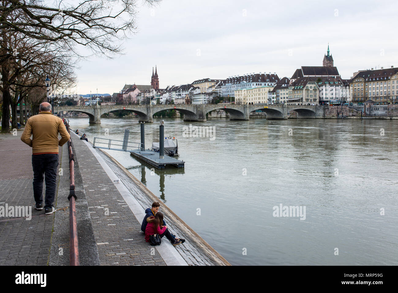 People on Basel riverfront opposite Basel's Altstadt (old town) on the footpath along the Rhine River. Stock Photo