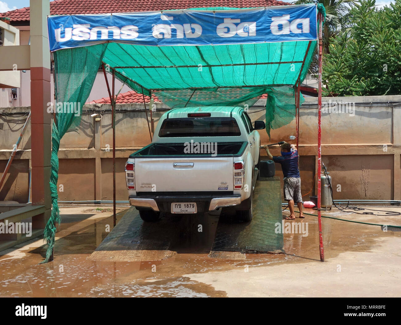 Urban outdoor car wash with workman washing a white pickup truck using a manually operated spray device, Udon Thani, Isaan, Thailand Stock Photo