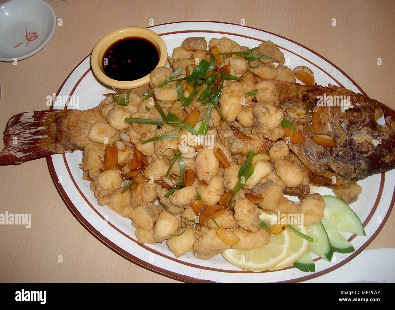 Fried fish cut into bite sizes and garnished with garlic and onions and assembled again in the plate to represent the whole fish. Stock Photo