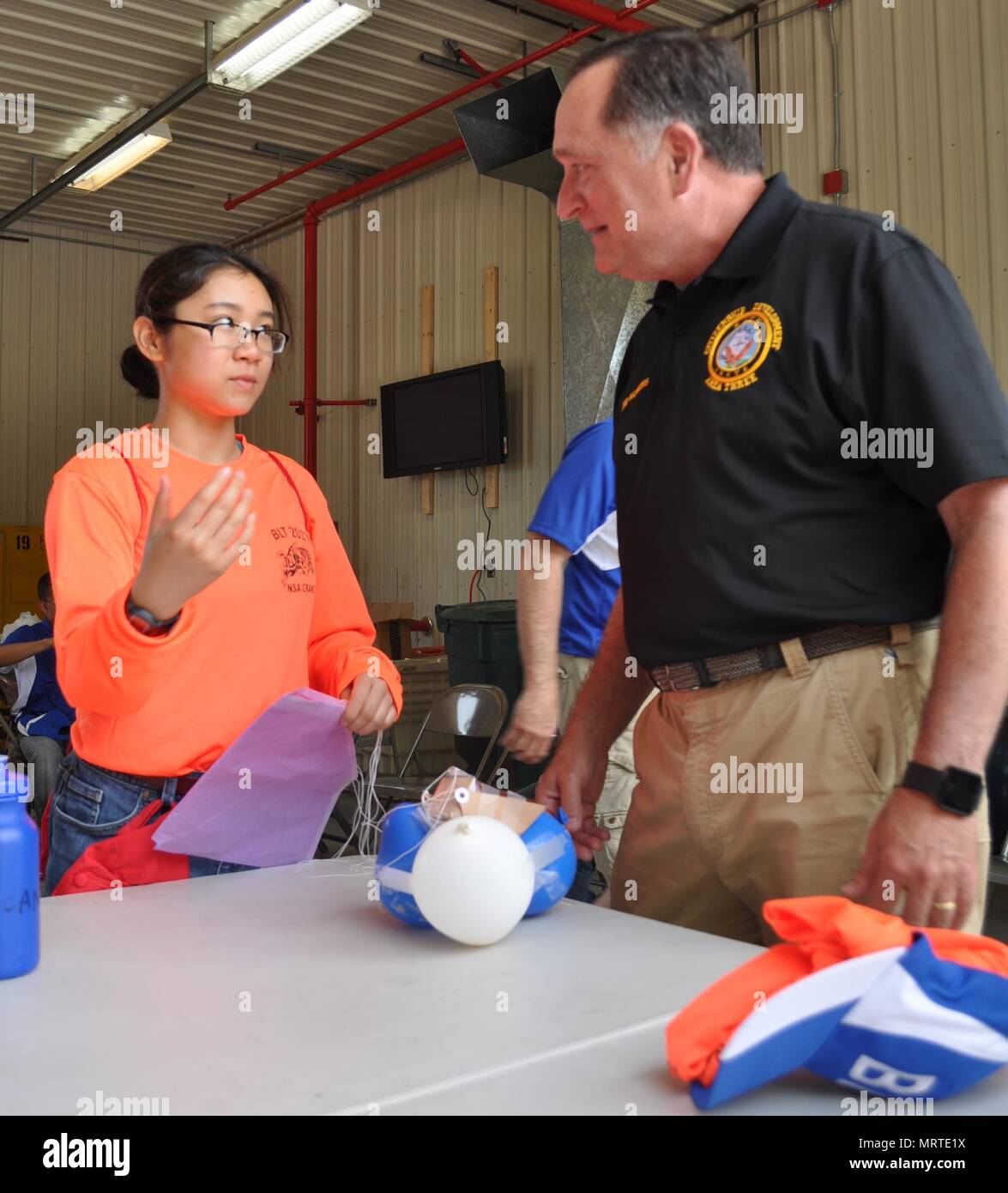 A Navy Junior ROTC student attending the Basic Leadership Training summer camp explains her team's egg drop project. Cadets worked together to create a contraption that would protect the egg during a drop from a three story building without breaking or cracking the egg after learning about the Mars Spirit Rover Landing. The BLT camp was held at Crane Army Ammunition Activity’s reserve facility located on Naval Support Activity Crane June 26-30. Stock Photo